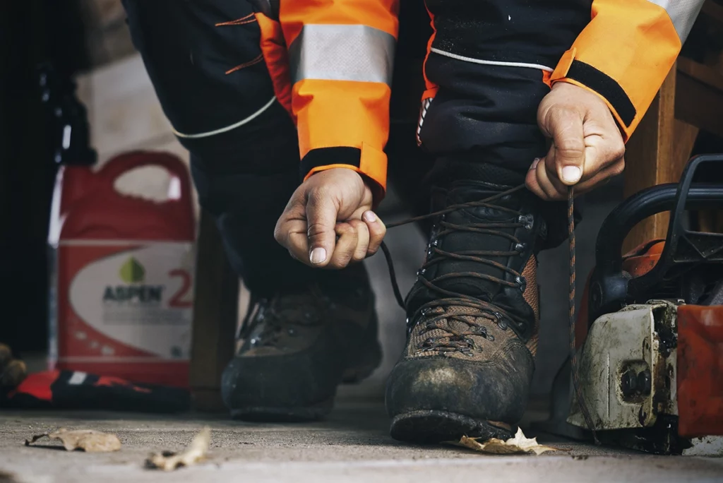 Man strikt zijn veters in de schuur waar een kettingzaag ligt met een can Aspen 2